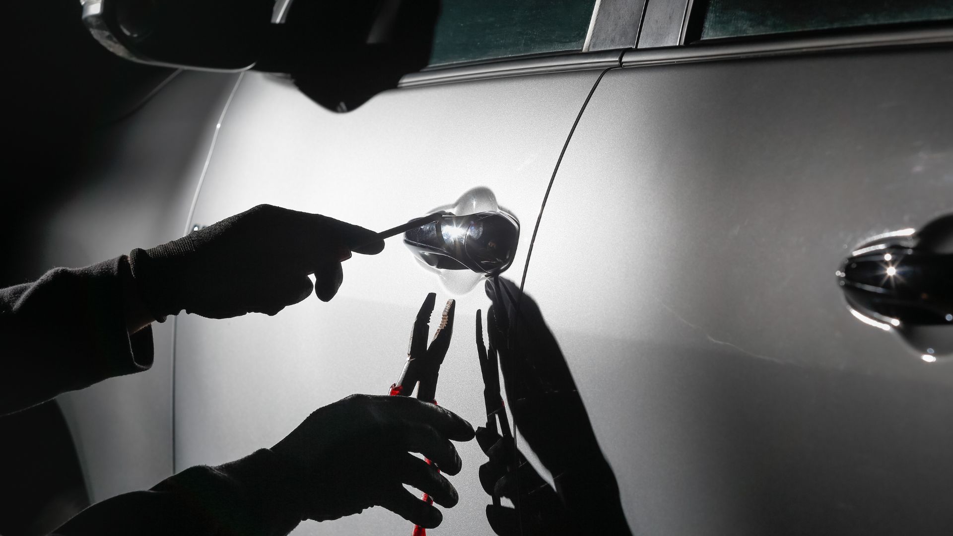 Auto wird gestohlen an der Tür ist eine Zange und ein silbernes graues Auto im Hintergrund