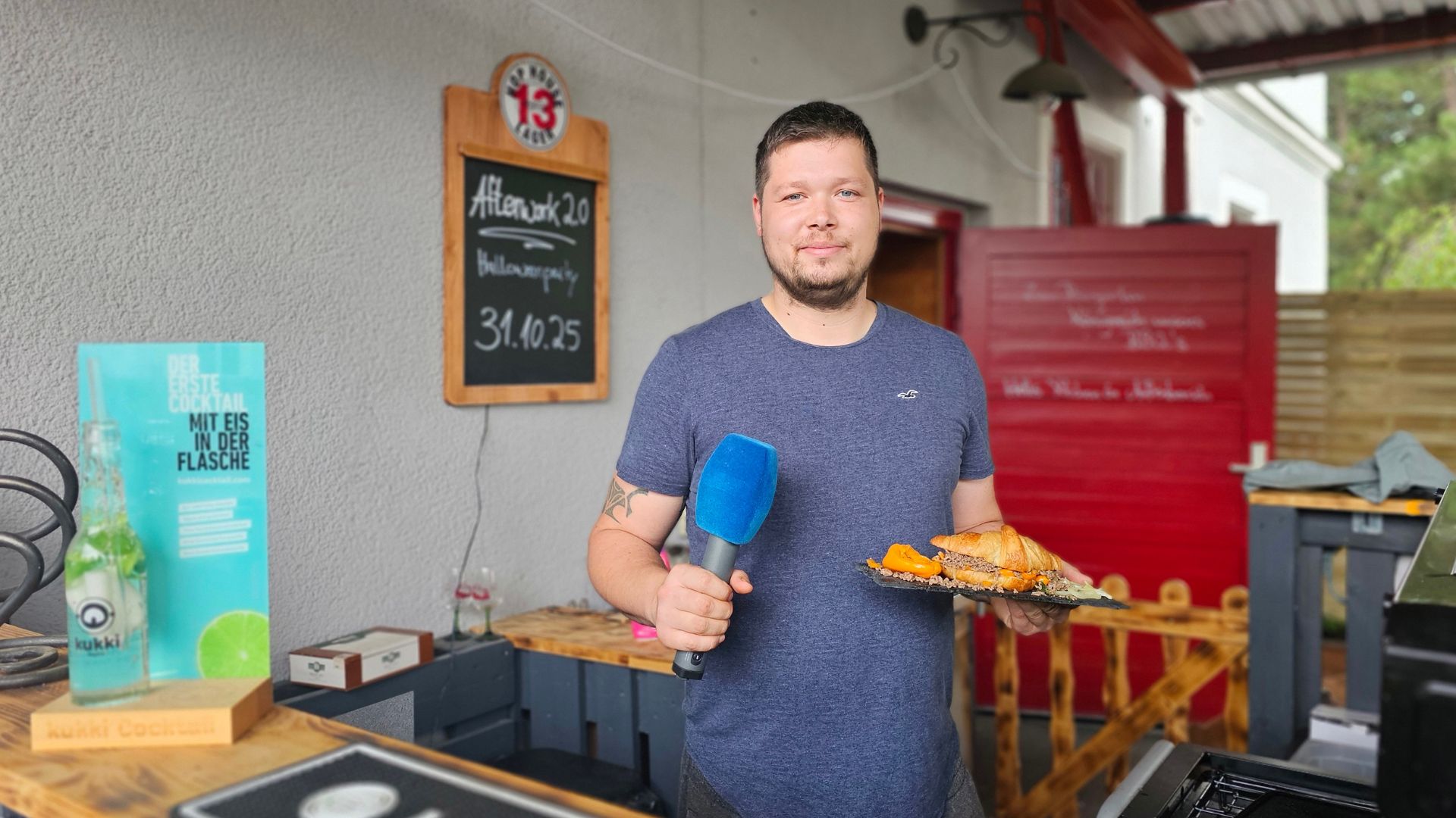 Robert Hantschel in seiner BBQ Outdoor Küche im Restaurant Lucifer BBQ Lounge mit einem Mikrofon in der Hand