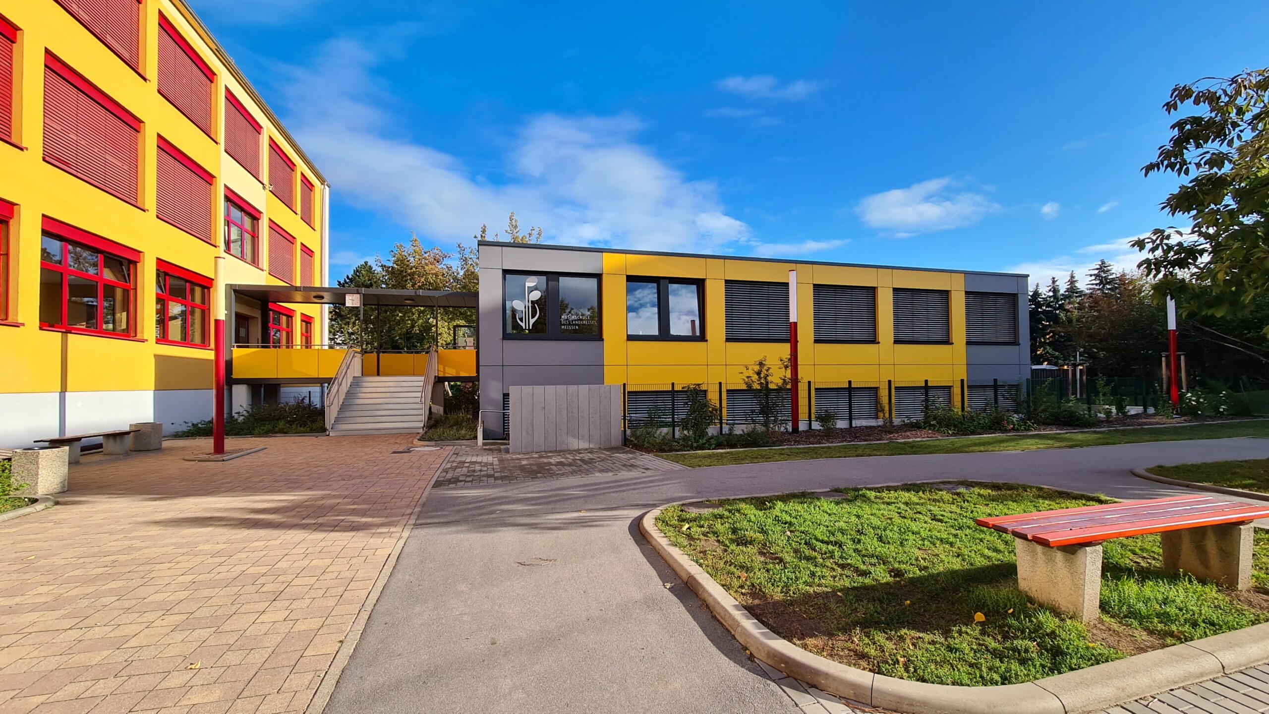 Musikschule in Coswig an einem sonnigem Tag im Vordergrund ist eine Bank und eine Wiese Rasenfläche
