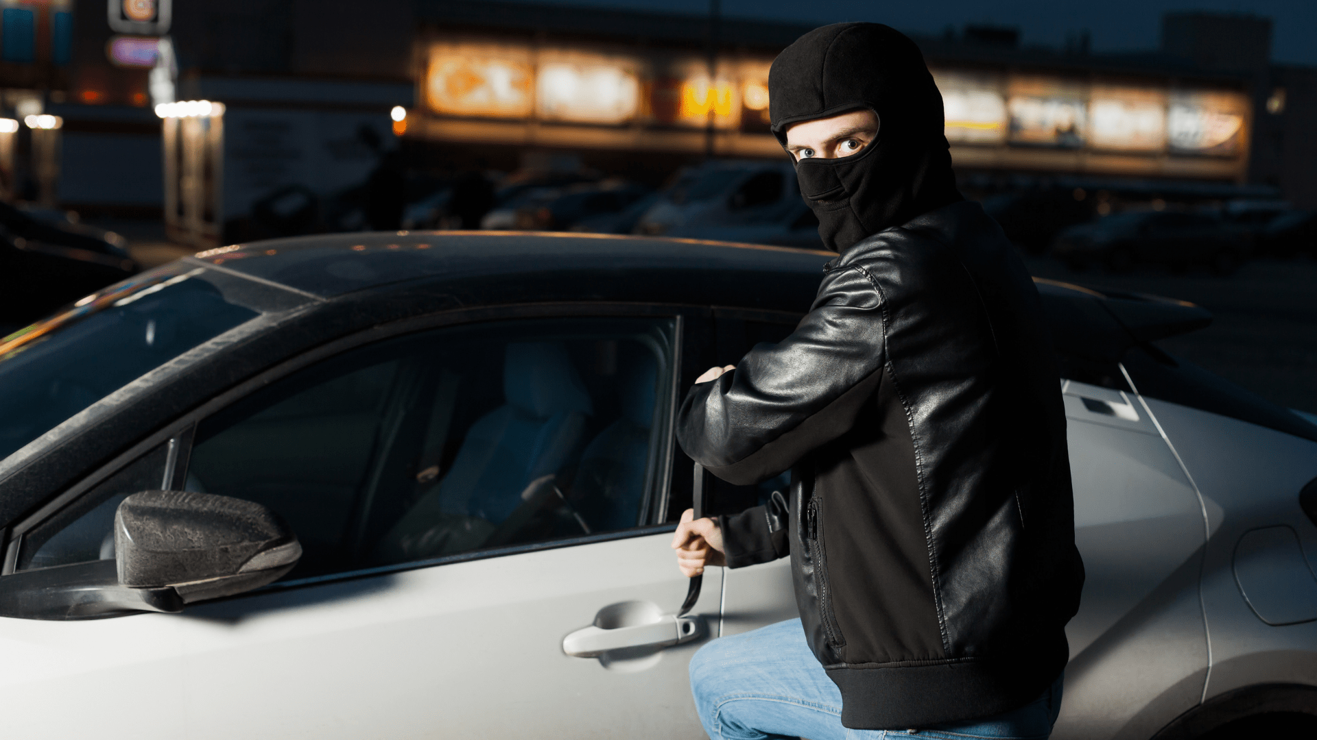 Ein Dieb mit einer Sturmhaube klaut ein weißes Sportauto mit einer Brechstange in der Hand