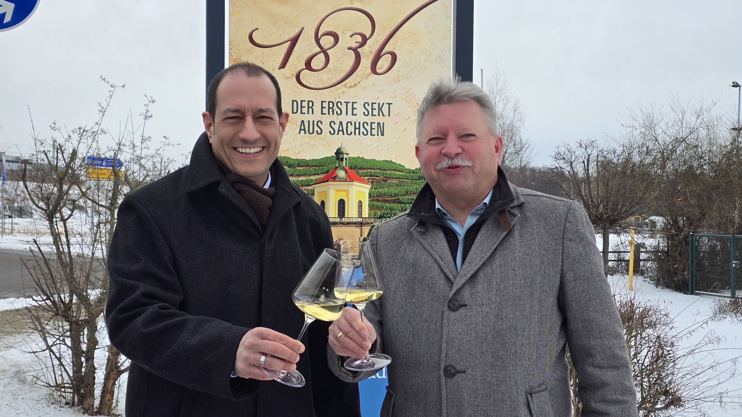 Jürgen Aumüller, Wein-Chef Schloss Wackerbarth, und OB Bert Wendsche stoßen an der neuen Stele auf das Sekt-Jubiläum 2026 an. Foto: © Branczeisz